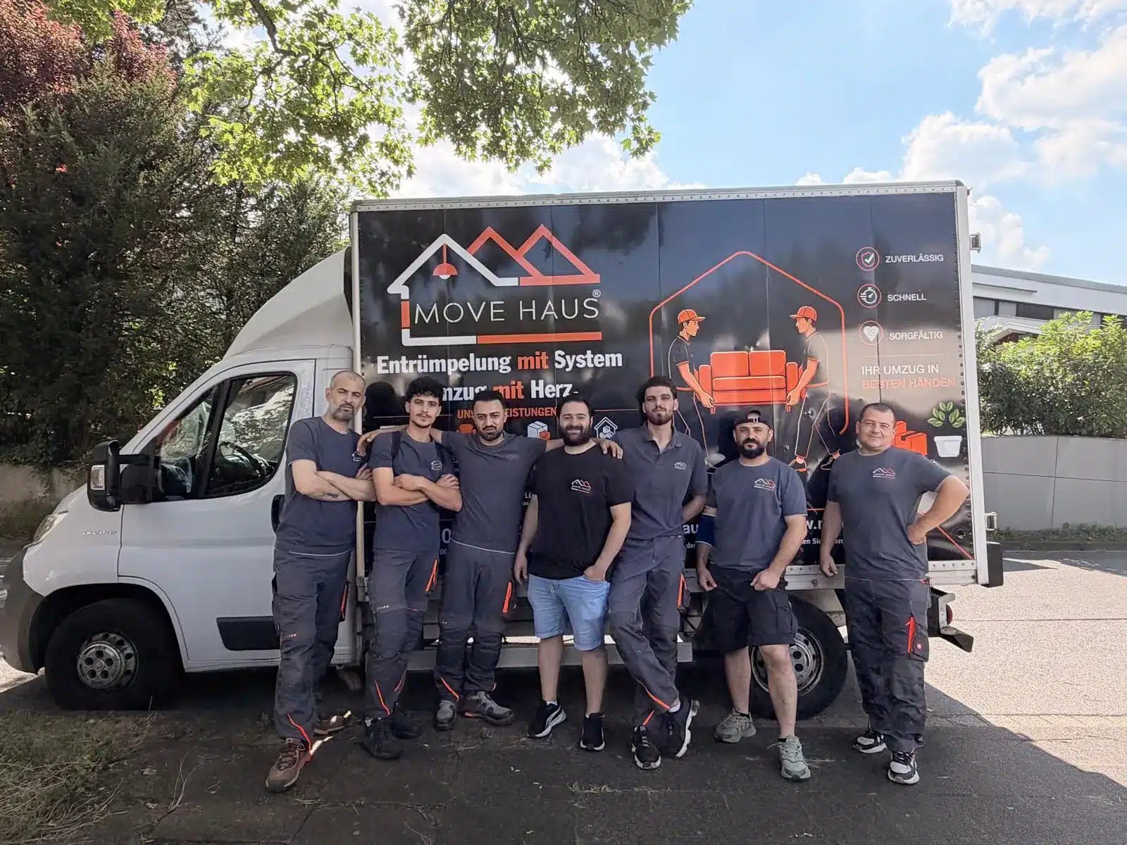 Umzugsunternehmen Bochum – das siebenköpfige Movehaus-Team in Arbeitskleidung vor dem eigenen beschrifteten Umzugswagen